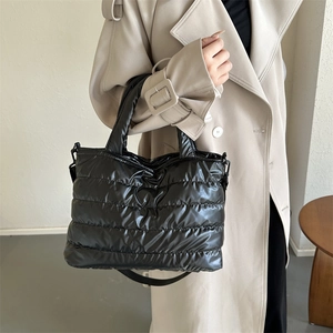 Chic black quilted puffer tote bag with handles and crossbody strap on a beige trench coat