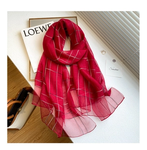 Detail of red checkered silk wool shawl with elegant lifestyle props on a white surface