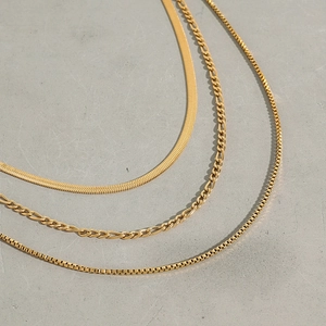 Detail of gold-plated snake, figaro, and box chain necklaces on a textured grey background