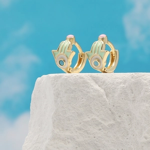 Golden Hamsa earrings with mint green and white enamel on a white stone background