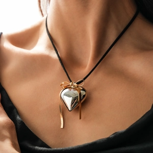 Polished silver heart pendant necklace with gold bow detail and black cord on model