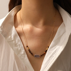 Close-up of gold chain necklace with tiger eye beads and rectangular shell pendant on neck