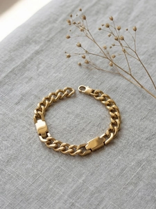 Detail of gold Cuban chain bracelet with polished ID tags on gray linen fabric