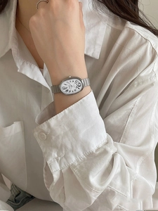 Close-up of minimalist silver steel strap watch with oval dial worn on a female wrist