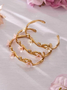 Detailed view of wave-shaped 18k gold plated bracelets with zircon flower motifs