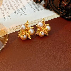 Detailed close-up of a gold bee-shaped earring with pearl accents on leather surface