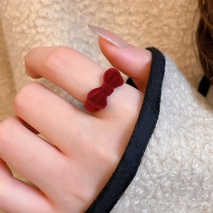 Detail of red velvet bow open ring worn on finger against cozy winter background