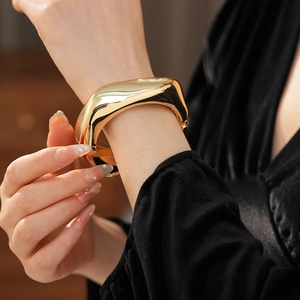 Close-up of a chunky golden irregular bangle with a high-polished mirror finish on wrist