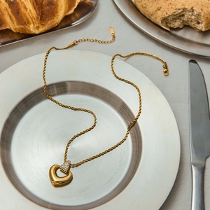 Détail d'un collier cœur doré orné de cristaux transparents sur une chaîne torsadée