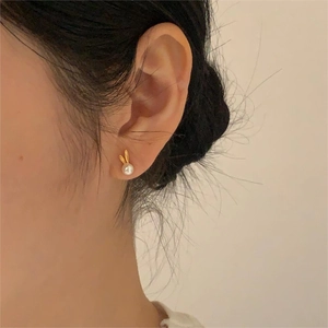 Close-up of golden bunny earrings with white pearl detail worn on model ear