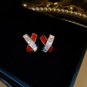 Detailed close-up of red enamel and gold criss-cross stud earrings with zircon stones