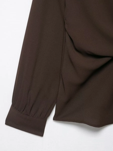 Detailed macro view of dark coffee crepe fabric texture and pleated sleeve cuffs on the shirt