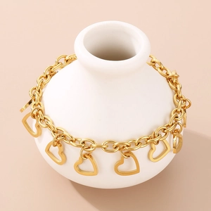 Chunky gold chain bracelet with hollow heart charms on a white ceramic display