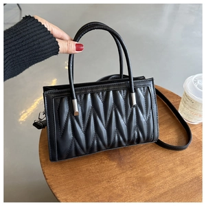 Detail of black quilted handbag featuring diamond pattern and metallic handle attachments