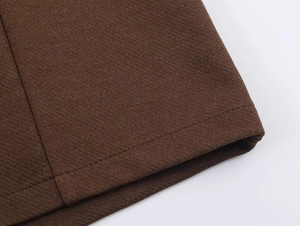 Close-up of dark brown woven fabric texture and neat stitching on jumpsuit hem