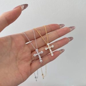 Detail of silver and gold cross pendants with small round diamonds held in hand