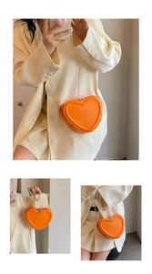 Detail der orangefarbenen herzförmigen Umhängetasche mit goldener Kette und Logo