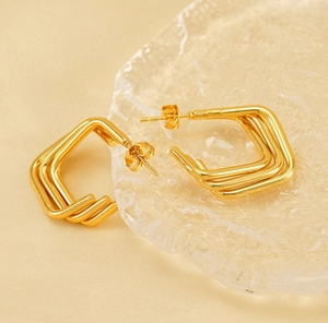 Gros plan de boucles d'oreilles en acier doré à triple couche sur verre texturé
