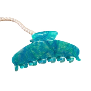 Pince à cheveux en acétate marbré bleu avec collier de perles sur fond blanc