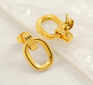 Détail de boucles d'oreilles ovales géométriques dorées sur un plateau texturé blanc