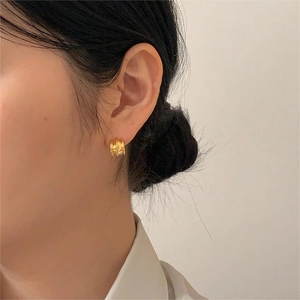 Macro view of gold hoop earring with vertical grooves worn by a model in soft light