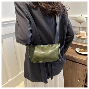 Detail view of dark green leather shoulder bag with blue pattern wide strap on model