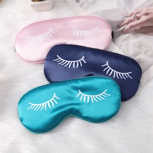 Three silk satin sleep masks with eyelash prints in pink, navy, and teal on plush background