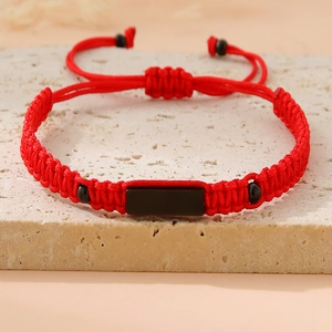 Detail of red and black woven bracelet with black rectangular plate on a stone background