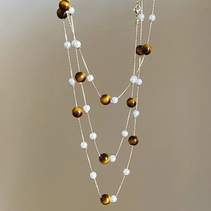 Detail of tiger eye beads and white pearls on a layered necklace with gold clasp