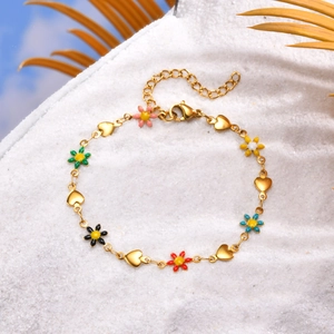 Detail of golden charm bracelet with colorful enamel flowers and heart on white sand