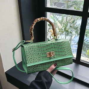 Detail of green faux-crocodile leather handbag featuring an authentic bamboo top handle