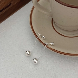 Close-up of polished silver dangle earrings with long chains on a beige ceramic cup