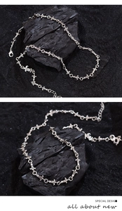 Detail of silver iris cross necklace links on dark charcoal and sand background