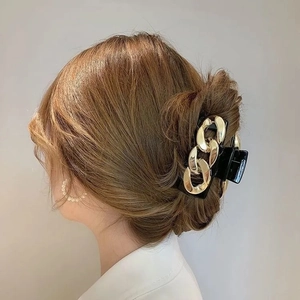 Close-up of golden chain design on black hair claw clip worn by a model for styling