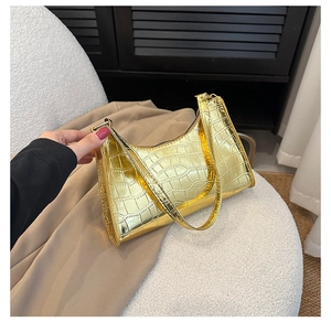 Detailed close-up of glossy gold crocodile pattern leather armpit bag on soft white seat