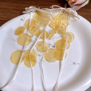 Close-up of yellow bamboo-style shell earrings with white ribbon bow on a ceramic plate