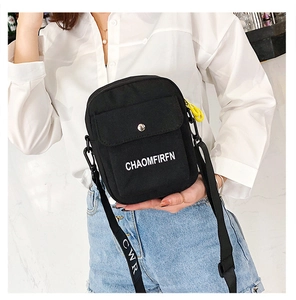 Detail of black canvas crossbody bag with white lettering and yellow clip detail