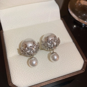Close-up of vintage zircon pearl earrings with silver crown design in a jewelry box