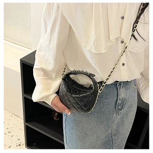 Detailed close-up of a small black quilted chain bag worn by a model in casual attire