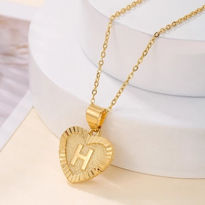 Macro shot of a gold heart pendant featuring an embossed letter H with sunburst texture