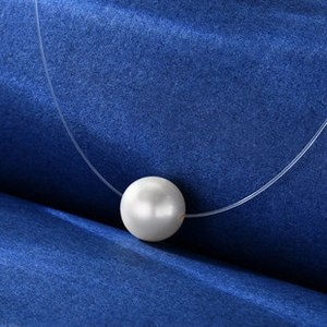 Detail of round freshwater pearl pendant on invisible line with blue velvet background