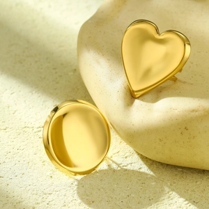 Minimalist gold heart and round stud earrings with a polished finish on stone background