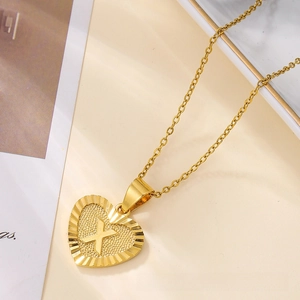 Close-up of gold heart pendant with embossed letter X and radial texture on chain