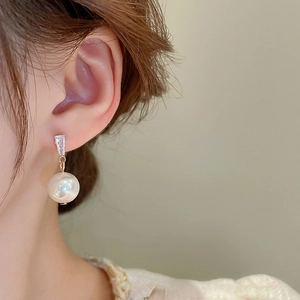 Detail of elegant pearl drop earring with rectangular diamond and gold finish on model