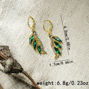 Macro view of gold leaf earrings with green gemstone and rhinestones on fabric