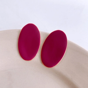 Close-up of minimalist burgundy oval earrings with gold trim on ceramic dish