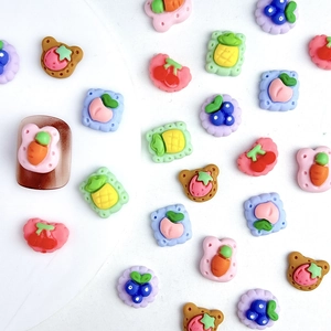 Flat lay macro of colorful resin fruit and animal shaped nail charms on white background