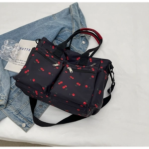 Detailed view of black nylon tote bag with red cherry print and front zipper pockets