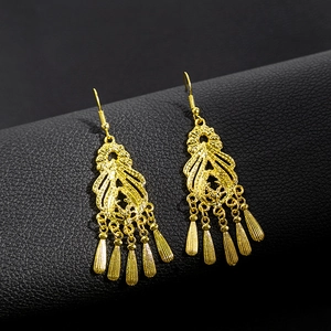 Detail of golden peacock earrings with hollow patterns and tassel pendants on black leather