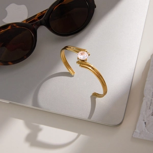 Gold plated stainless steel open bangle featuring a large round zircon stone centerpiece
